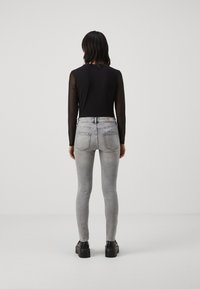 Čierny top s dlhým rukávom a priesvitnými rukávmi v kombinácii so svetlosivými vysokými skinny džínsami, ktoré majú hladkú textúru a zadné vrecká.