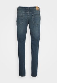 Blue denim jeans with a slim fit, five pockets, and a brown leather brand patch on the waistband. Features a smooth texture and straight legs.