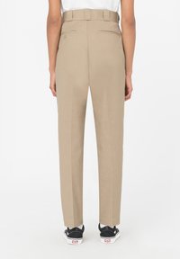 Beige kalhoty s vysokým pasem a rovnou nohavicí, s poutky na opasek a dvěma zadními kapsami. Nosené s černými teniskami.