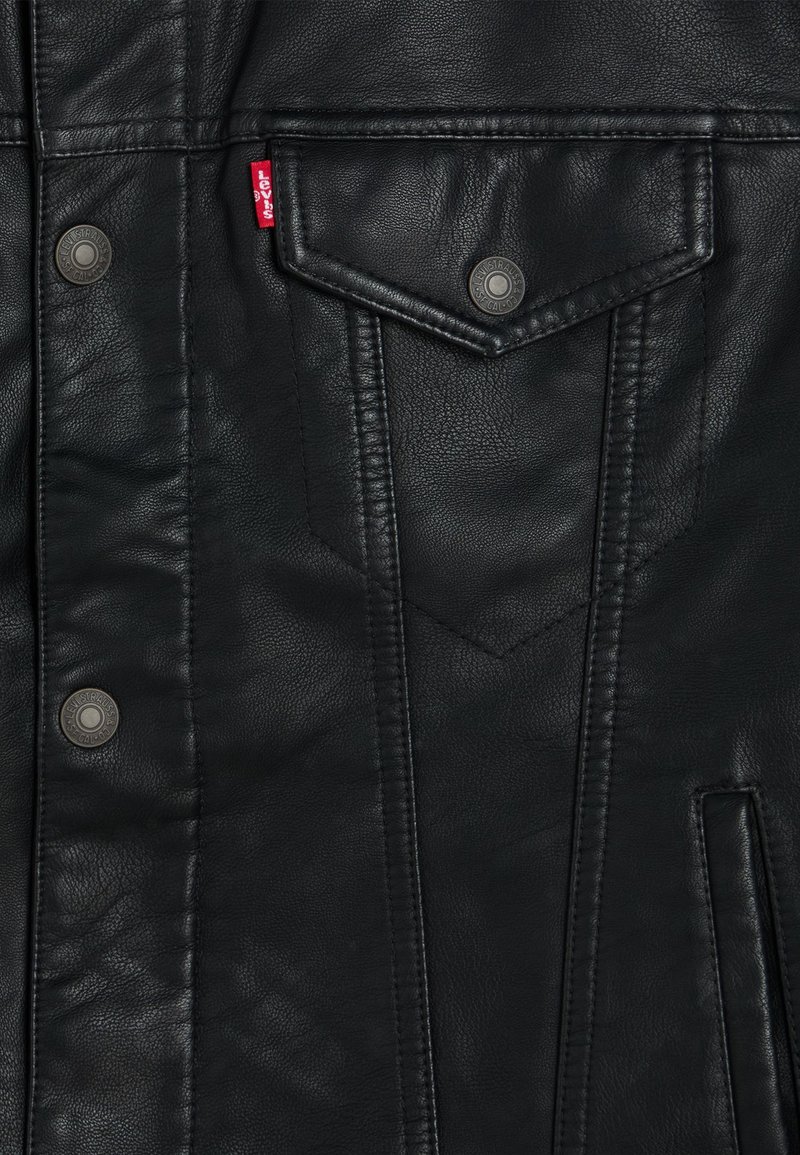Veste en cuir noir avec des boutons-pression et une poche poitrine. Surface texturée avec des coutures visibles et une petite étiquette de logo.