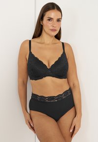 Musta pitsinen rintaliivi, jossa on tukikaaria, kukkakuosisena ja säädettävillä olkaimilla. Mustat korkeavyötäröiset alushousut, joissa on pitsireunus.