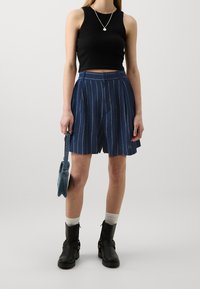 Czarny krótki top, niebieskie szorty w paski, czarne botki za kostkę i mała torba dżinsowa. Strój charakteryzuje się luźnym fasonem i warstwowymi fakturami.