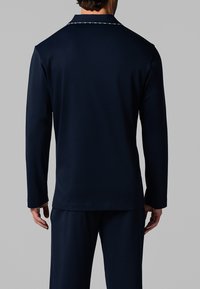 Camicia a maniche lunghe blu navy con colletto tondo, caratterizzata da dettagli in cucitura bianca. Realizzata in tessuto liscio, progettata per adattarsi comodamente.