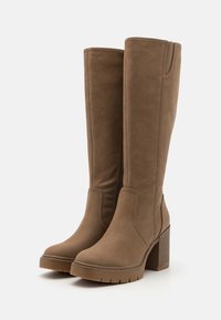 Bottes marron jusqu'au genou en matériau synthétique texturé, avec un talon bloc et des zippers latéraux pour un enfilage facile. Semelle épaisse.