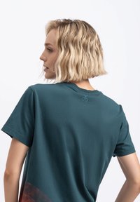 Teal korte mouw t-shirt gemaakt van zachte katoen; heeft een ronde halslijn en een klein logo op de hals aan de achterkant. Kenmerkend kleurcontrast aan de zoom.