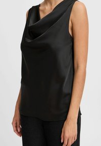 Top senza maniche nero in tessuto liscio e lucido con scollo drappeggiato. Presenta una vestibilità rilassata e un orlo curvo. Abbinato a pantaloni scuri con texture.