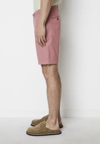Pink cotton shorts with a straight cut, side pockets, and a buttoned back pocket. Worn with brown suede slip-on shoes.