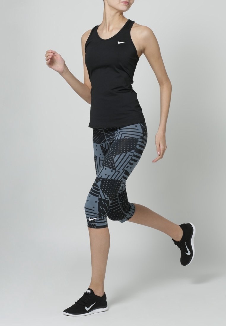 Czarny sportowy tank top, legginsy capri w szaro-czarny wzór z geometrycznymi motywami i kropkowanymi akcentami, czarne sportowe buty.