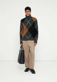 Πλεκτό πουλόβερ με λαιμόκοψη σε γκρι, μαύρο και καφέ χρώμα με διαμαντένιο σχέδιο; συνδυασμένο με μπεζ παντελόνι και μαύρη δερμάτινη τσάντα.