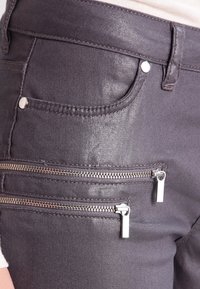Jeans de denim gris oscuro con un ligero brillo, que cuentan con dos bolsillos con cremallera en la parte frontal y costuras estándar.