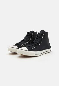 Zapatillas altas negras de lona, con punta de goma blanca y cordones negros. Presentan rayas blancas en la suela y un detalle del logo.