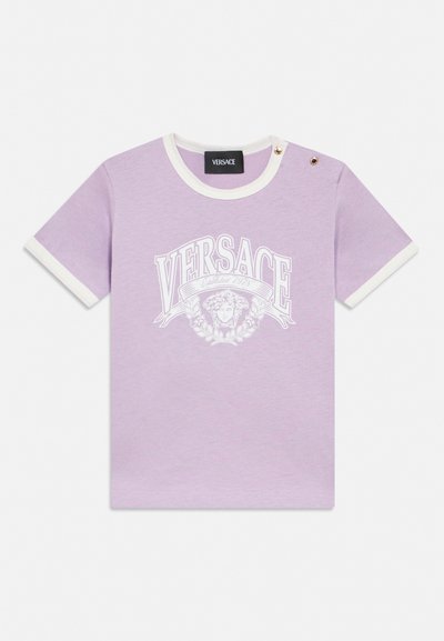 T-shirt en coton lilas à manches courtes avec bordure blanche, deux boutons dorés aux épaules et logo Versace blanc avec graphique de tête de Méduse sur le devant.