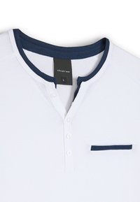 Biała koszulka henley z krótkim rękawem, z granatowym żebrowanym kołnierzykiem, dwoma guzikami z przodu oraz małą granatową kieszonką, wykonana z miękkiej bawełny.