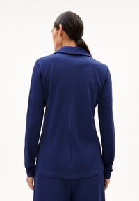 Donkerblauwe lange mouw polo met een puntige kraag, zachte textuur en een centrale naad op de rug.