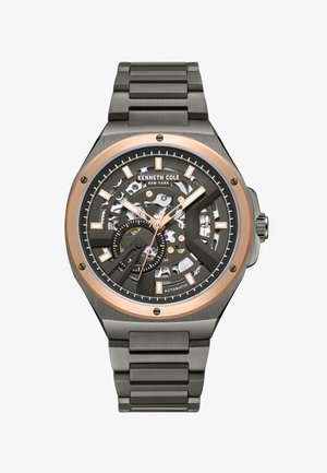 Automatisk klocka med en svart skelettskiva och roséguldfärger, en klocka i rostfritt stål och armband samt vinklade timmarkörer.