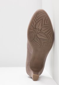 Semelle d'une chaussure à talon haut en daim beige avec un motif floral sur la semelle, taille 37, et le nom de la marque "bugatti" embossé sur la semelle.