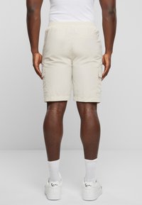 Beige cargo-shorts med elastisk midje, sidelommer, og en avslappet passform, kombinert med hvite sneakers og ankelsokker.