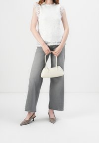 Vit spetsblus med scallopkanter, grå vida jeans, ljusgrå slingback-skor och en liten handväska i krämfärg. Släta textila ytor.