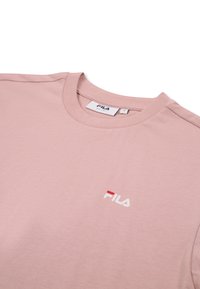 T-shirt in cotone color rosa chiaro con scollo tondo, con logo FILA rosso e bianco nella zona sinistra del petto, texture liscia e maniche corte.