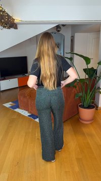 Flared black pants with a textured, shiny finish, paired with a black t-shirt. Features a wide waistband and relaxed fit. Indoor setting.