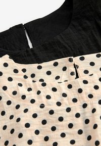 Zwarte en beigekleurige jurk met een ronde halslijn, zwart bovenstuk en een beige onderstuk versierd met zwarte stippen.