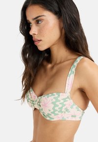 Green bikini with large pink floral patterns, gathered detailing at the center, and wide shoulder straps. Smooth fabric texture.