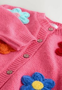 Cardigan en tricot rose avec de grandes fleurs texturées en bleu, orange et rouge, boutons ronds en bois le long du devant.