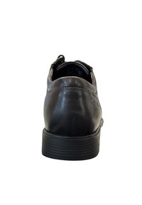Zapato de vestir de cuero negro con tacón redondeado, textura suave y suela de goma con ranuras horizontales. Marca sutil en el lateral.