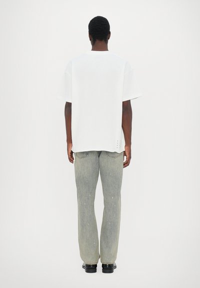White short-sleeve t-shirt, relaxed fit, paired with light gray jeans featuring subtle star patterns and a straight leg design. Black shoes.