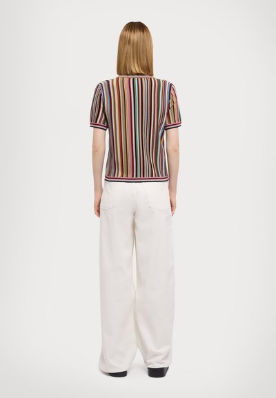 Haut tricot à rayures à manches courtes avec des lignes verticales multicolores, finitions côtes, porté avec un pantalon large blanc, mettant en valeur une coupe décontractée.