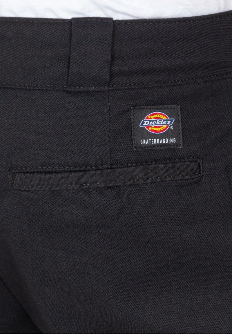 Schwarze Dickies Skateboard-Hosen mit einer Gesäßtasche und einem quadratischen Etikett, das ein buntes Logo und Text zeigt. Hergestellt aus strapazierfähigem Material.