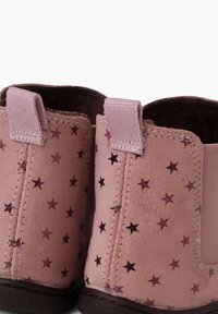Botas de tobillo de ante rosa con patrones de estrellas púrpuras en relieve, paneles laterales elásticos y lengüetas en la parte posterior para facilitar su puesta.