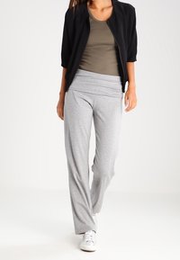 Chaqueta bomber negra, camiseta sin mangas verde olivo, pantalones de corte relajado gris claro, textura suave, combinando con zapatillas blancas.