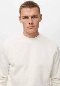 Sudadera blanca con cuello redondo, que presenta una textura suave y mangas largas. La tela parece suave y casual.