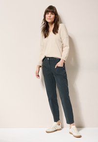 Beige knit sweater, relaxed fit, V-neck; dark gray tapered pants with side pockets; light sneakers with beige and brown accents.