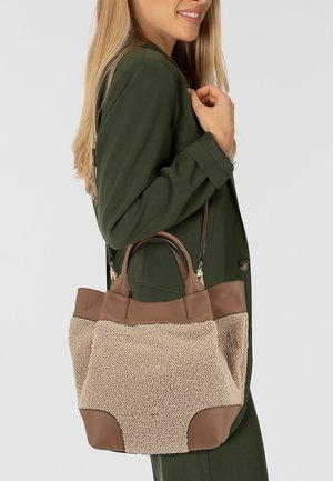Sac en cuir marron et fausse fourrure beige avec des poignées doubles et une bandoulière amovible, présentant une forme structurée et des textures contrastées.