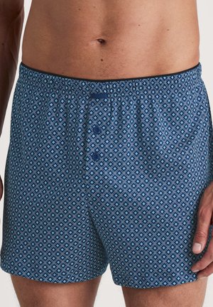 Blaue gemusterte Boxershorts mit geometrischem Design, elastischem Bund und drei Knöpfen vorne. Hergestellt aus leichtem Stoff.