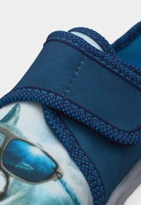 Chaussure bleue pour enfant avec bride en Velcro et un chien portant des lunettes de soleil bleues imprimé sur la tige en tissu.