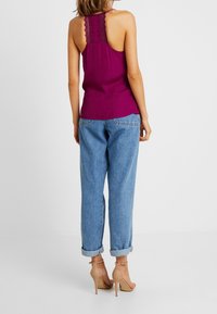 Top in viola con dettagli in pizzo sul retro, abbinato a jeans azzurri arrotolati e sandali con tacco beige.
