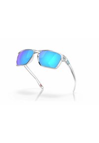 Gafas de sol con un marco rectangular transparente y lentes azules espejados. Las patillas ligeras tienen un pequeño acento de logo rojo.