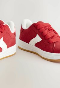 Røde ruskindsneakers med hvide detaljer, runde snørebånd og en tekstureret gummisål; blød hvid foring indeni for komfort.