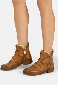 Braune Leder-Ankelstiefel mit lässigem Design, goldenen Reißverschlüssen und durchbrochenen Mustern. Flache Sohle und runde Zehen sorgen für einen lässigen Look.