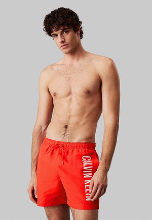 Shorts da bagno rossi con vita elasticizzata, cordino e logo "CALVIN KLEIN" stampato verticalmente sul lato sinistro.