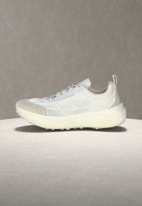 Chaussure de sport blanche avec semelle épaisse et dessus en tissu mesh, vue de profil sur fond neutre.