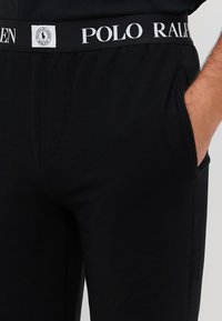 Czarne dresy z białym logo w pasie z napisem "POLO RALPH LAUREN". Wykonane z miękkiego materiału, zaprojektowane z bocznymi kieszeniami i luźnym krojem.