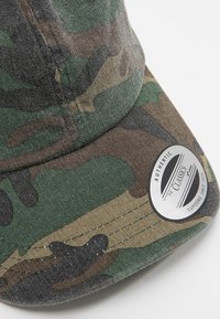 Căciulă cu model camuflaj, cu vizor curbat, fabricată din material din bumbac. Prezintă o insignă rotundă și detalii de cusătură vizibile.