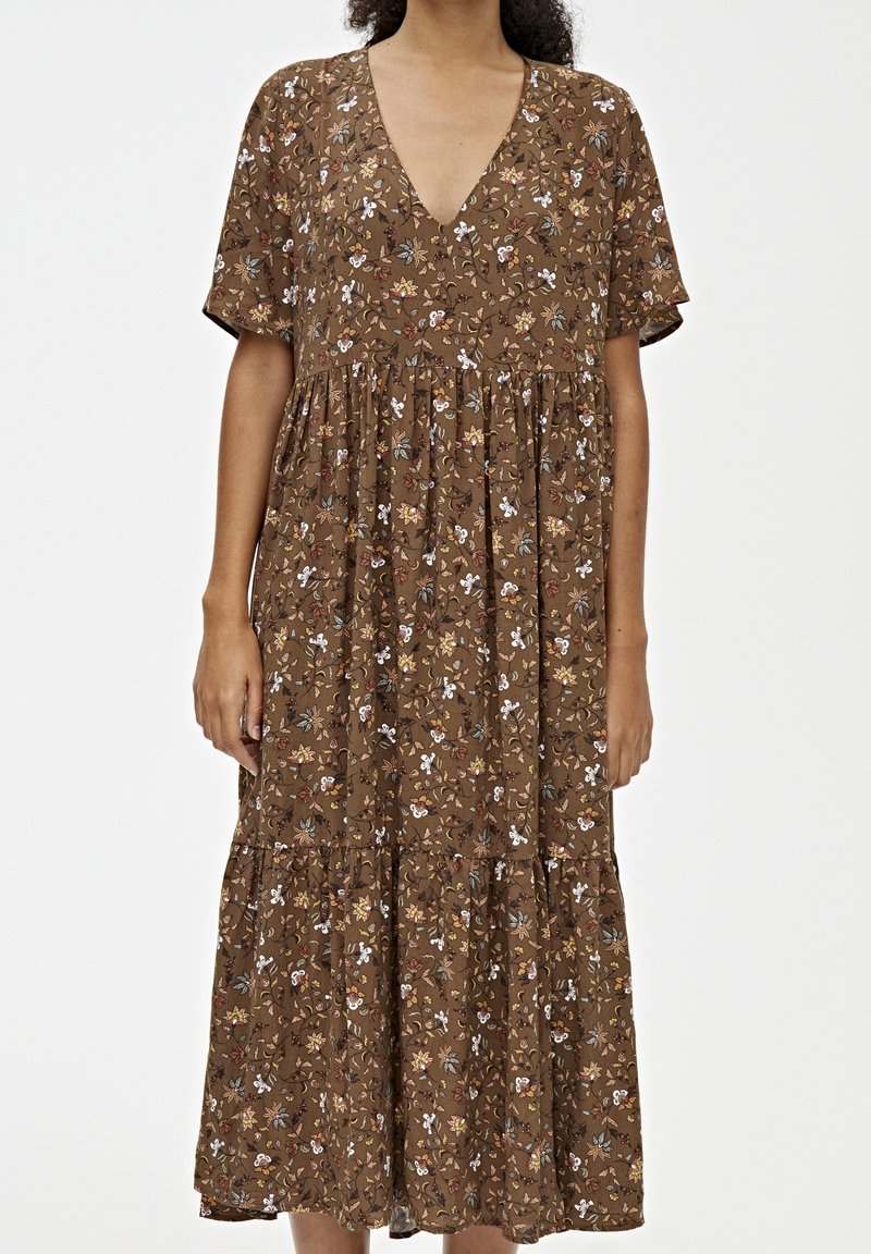 Robe maxi marron à manches courtes avec un col en V et un petit imprimé floral aux tons blancs, jaunes et verts.