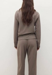 Felpa in cotone marrone e pantaloni abbinati, con una vestibilità comoda. La felpa presenta un taglio corto e maniche lunghe; i pantaloni hanno un cinturino elasticizzato.