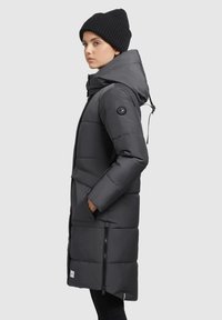 Long, black puffer coat with a hood and side zipper pockets. Features a quilted design and circular logo accent on sleeve.