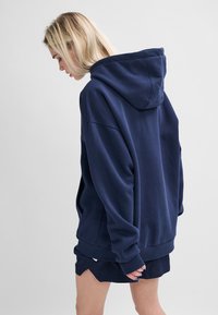 Marinblå oversized hoodie med dragsko i huvan, sänkta axlar och ribbade muddar, kombinerad med matchande shorts. Mjuk textur.